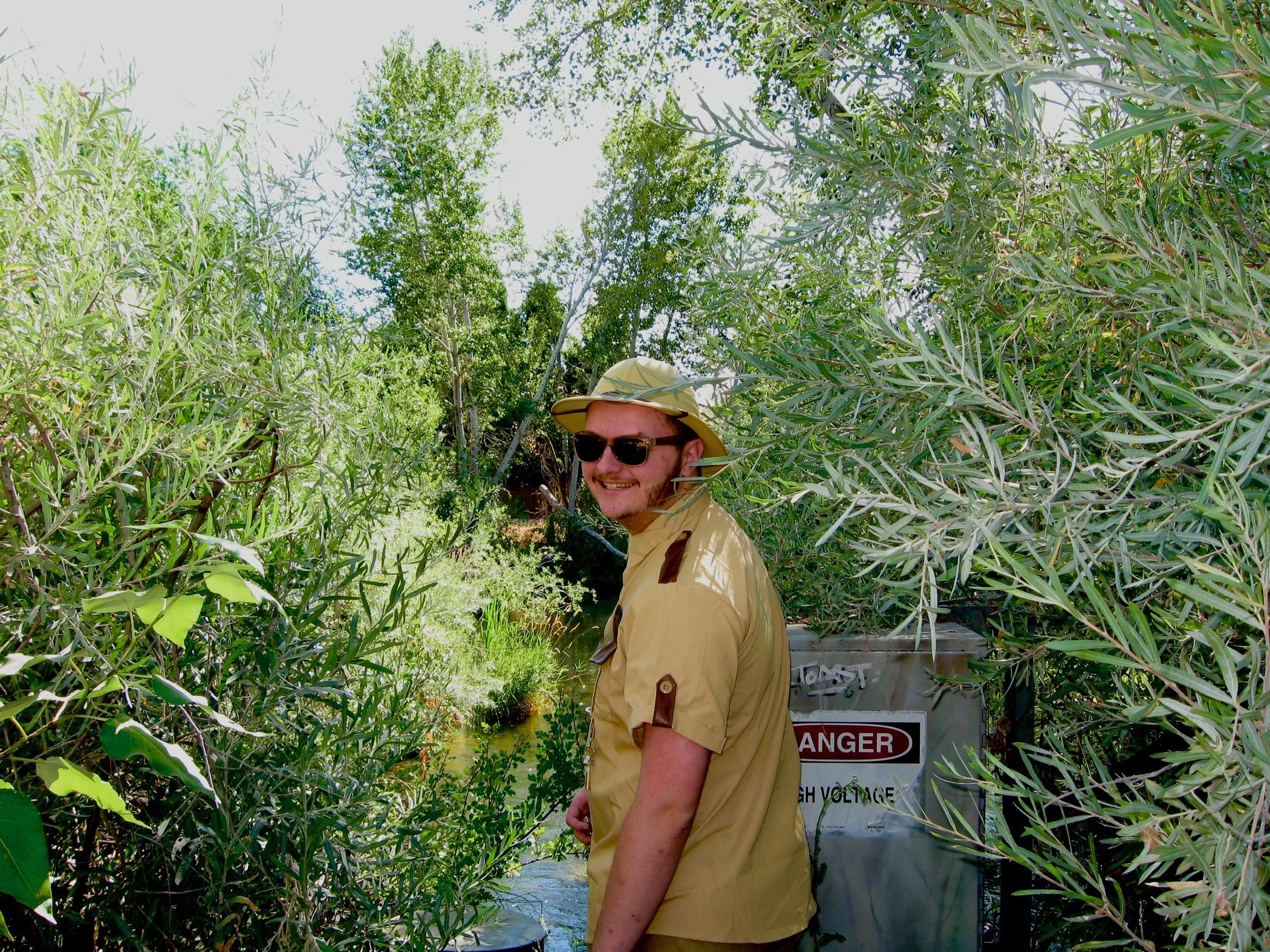 Daughter Lotus wearing sunglasses and a safari uniform, smiling and looking towards the camera, while the rest of his body is facing away from the camera