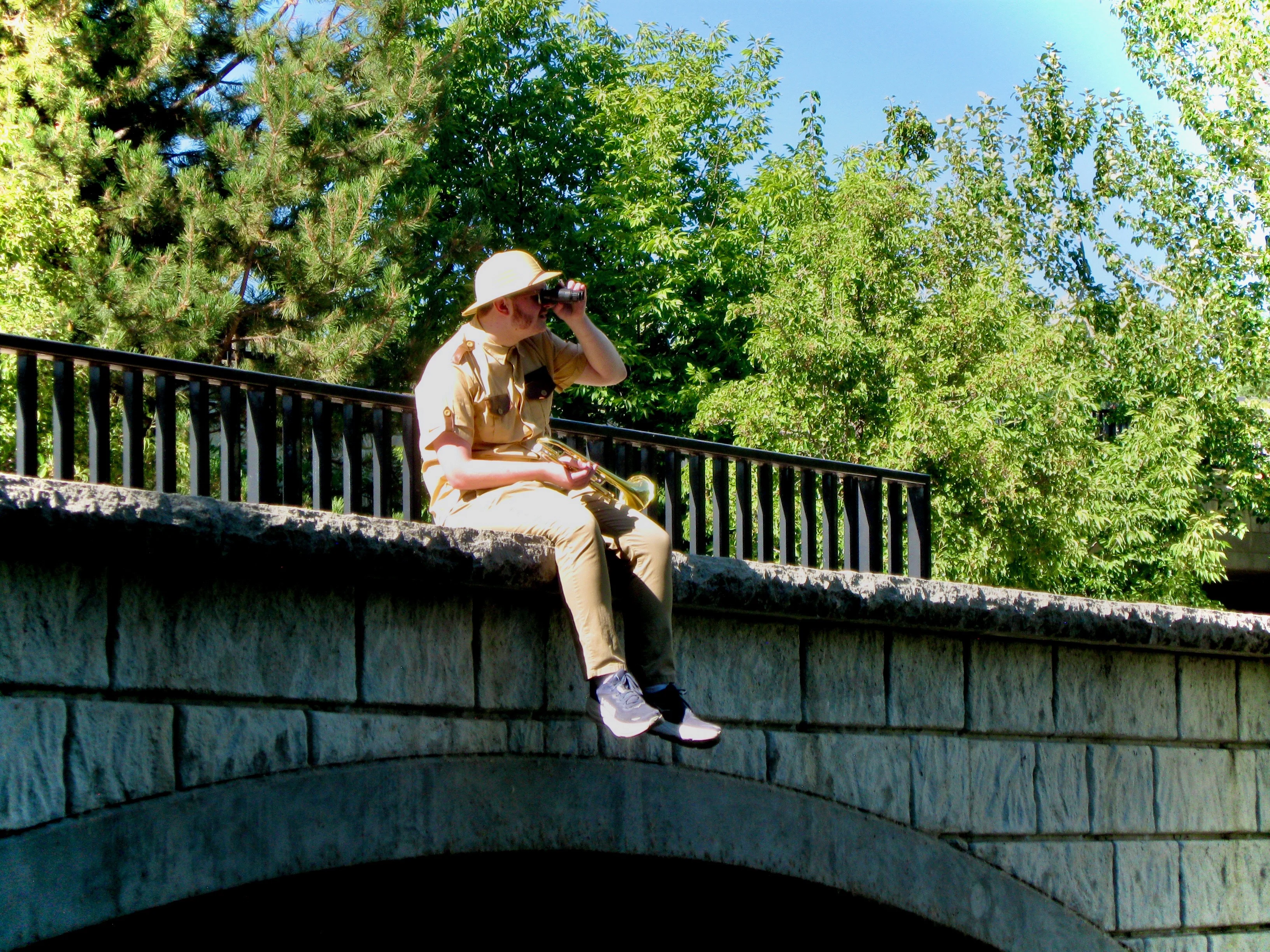 Daughter Lotus wearing sunglasses while sitting on a bridge and looking to the right in the distance through binoculars.
