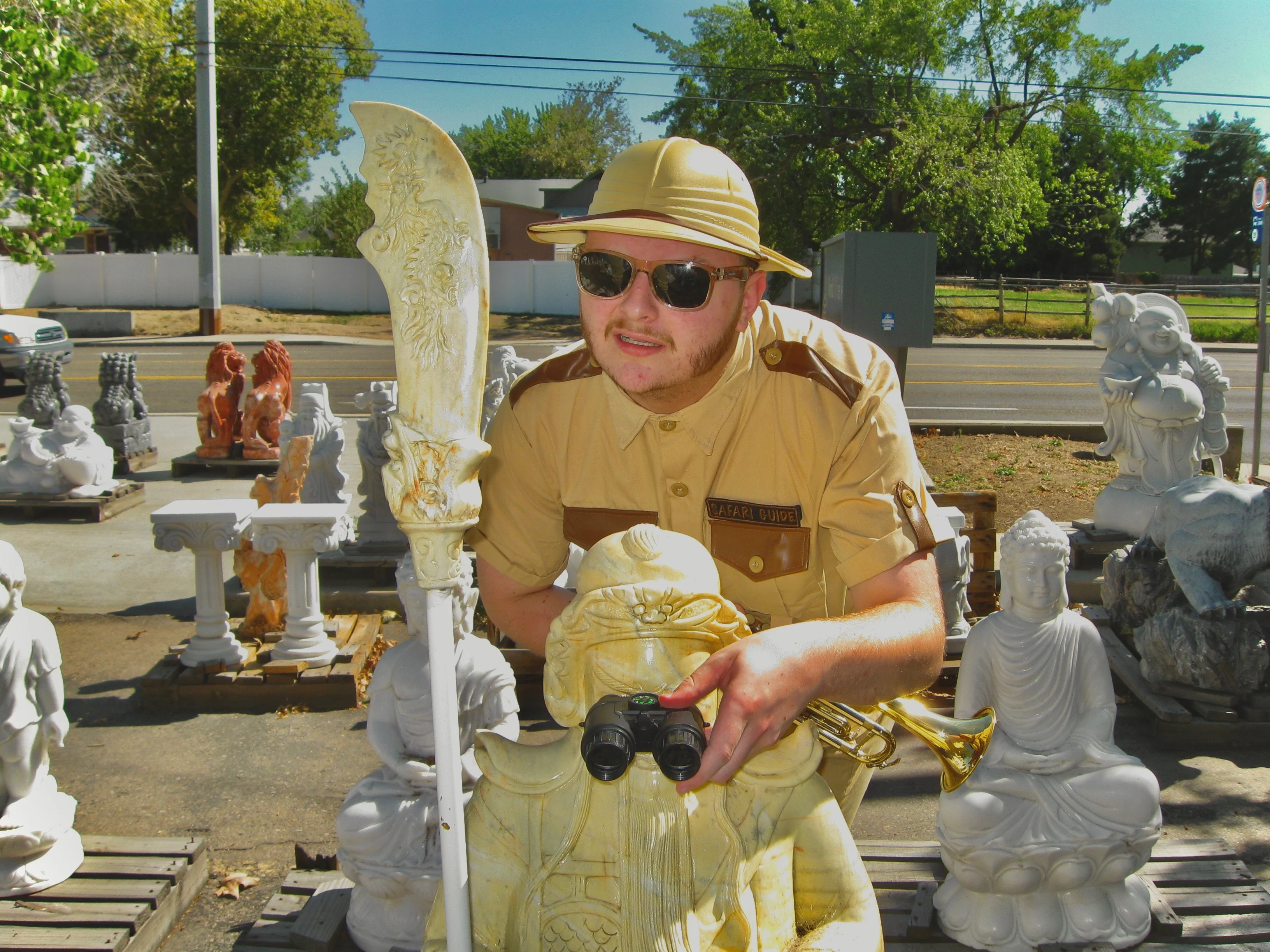 Daughter Lotus, wearing a safari uniform and sunglasses, placing binoculars in front of a statue's eyes to make it look as if the statue is looking through them.