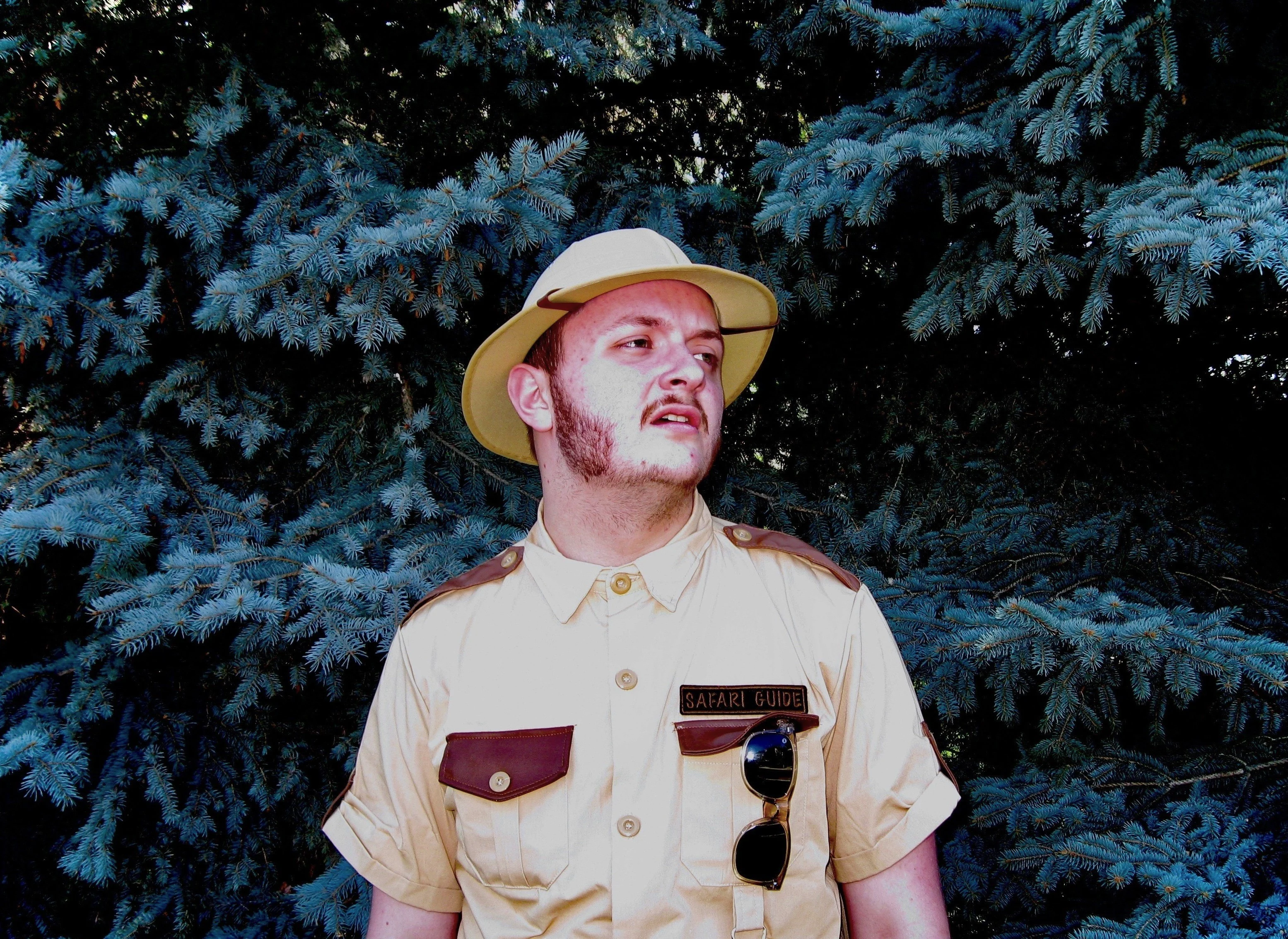 Daughter Lotus, wearing a safari uniform, standing in front of dark-blue fir trees.